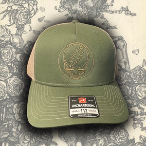 May include: Green and beige trucker hat with a brown embroidered Grateful Dead logo. The hat has an adjustable strap and a label that reads "Richardson 112 Original Trucker Adjustable".