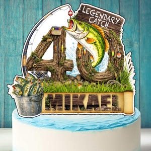 Peut inclure: Un gâteau avec un décor sur le thème de la pêche. Le décor comprend un grand poisson vert et jaune sautant hors de l'eau, une canne à pêche et les mots "Legendary Catch". Un seau de poissons et le nom "MIKAE" sont également inclus.
