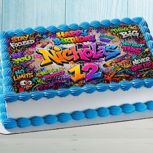May include: A rectangular birthday cake with blue frosting trim and a white base. The cake is decorated with a colorful graffiti-style design that says "Happy Birthday Nicholas 12" with motivational phrases.