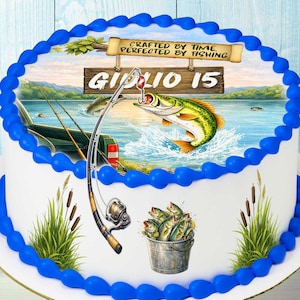Può includere: Una torta rotonda decorata con un tema di pesca. La torta presenta un'immagine dettagliata di un pesce che salta fuori dall'acqua, una canna da pesca e un secchio di pesci. La torta è decorata con glassa blu sui bordi e ha il testo "Crafted by Time, Perfected by Fishing."