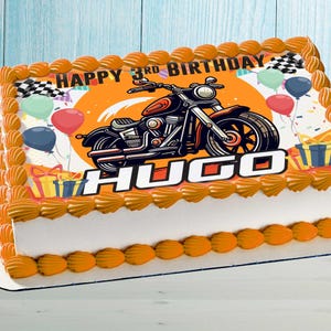 Könnte beinhalten: Ein rechteckiger Blechkuchen mit orangefarbenem Zuckergussrand und einem Aufdruck eines Motorrads, bunten Luftballons, Geschenken und Zielflaggen. Der Text lautet HAPPY 3RD BIRTHDAY und der Name HUGO in großen weißen Buchstaben.