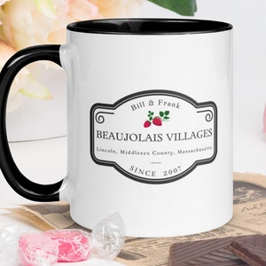 Peut inclure: Une tasse à café en céramique blanche avec un bord et une poignée noirs. La tasse présente un logo noir et blanc avec le texte "Bill & Frank Beaujolais Villages Lincoln, Middlesex County, Massachusetts Since 2007".