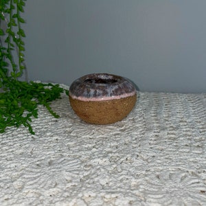 May include: A small, round ceramic planter with a brown, speckled exterior and a white and pink glaze on the rim.