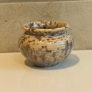 May include: A small, brown and cream ceramic pot with a mottled glaze. The pot has a rounded shape and a slightly flared rim.