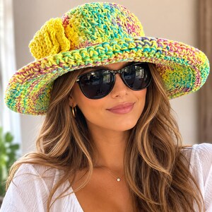 May include: A wide-brimmed crochet hat featuring a vibrant multicoloured yarn pattern in shades of yellow, green, blue, and pink. The hat is adorned with a large, solid yellow crocheted flower accent on the side and has a structured, rounded crown.