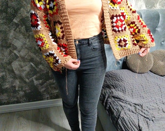May include: A crocheted cardigan with a brown base and colorful squares in red, yellow, and white. The cardigan has a loose fit and a long, open front.