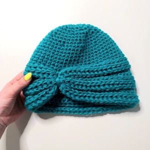 May include: A teal blue crocheted beanie with a knotted bow detail.