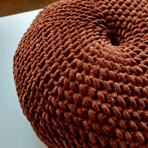 May include: A brown knitted pouffe with a circular shape and a textured surface.