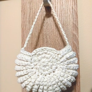 Op de afbeelding: Een witte gehaakte handtas met een gegolfde rand en een eenvoudig, geweven handvat.