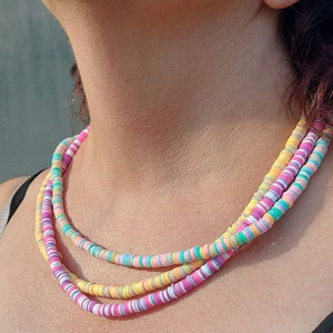 Peut inclure: Un collier multi-rangs composé de trois couches de petites perles d'argile plates et circulaires dans une palette vibrante de rose pastel, jaune, turquoise, lavande et blanc. Les perles sont enfilées pour créer un accessoire superposé.