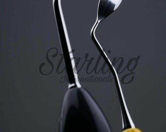 May include: Close-up of two dental tools. One tool has a black handle and a curved, silver metal end. The other tool has a yellow handle and a spoon-shaped, silver metal end. The tools are set against a dark grey background.
