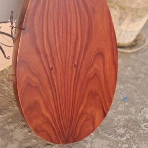 May include: A wooden, teardrop-shaped planter with a rich, reddish-brown finish. The wood grain is prominently displayed, creating a natural, textured appearance. The planter is partially filled with green plants.