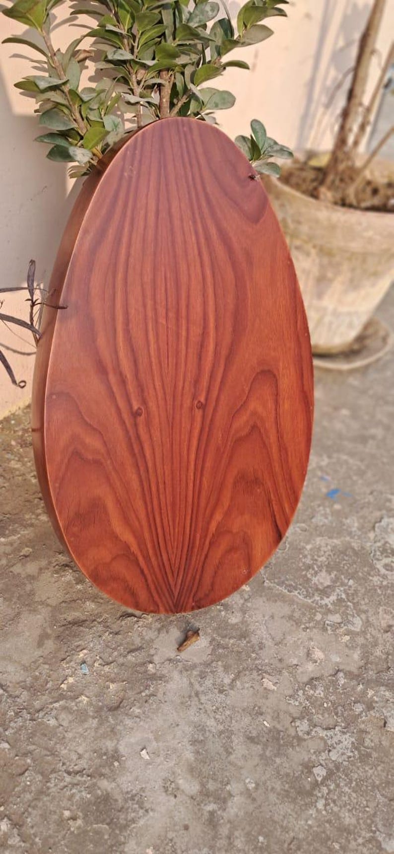 May include: A wooden, teardrop-shaped planter with a rich, reddish-brown finish. The wood grain is prominently displayed, creating a natural, textured appearance. The planter is partially filled with green plants.