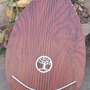 May include: A wooden musical instrument with a teardrop shape. The instrument has many strings and a decorative tree design in the centre. The body is a reddish-brown colour, and the strings are silver.