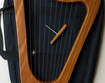 May include: A wooden harp with a rich, brown finish, featuring multiple strings and tuning pegs. The instrument is placed on a black carrying case. A tuning tool is also present. The harp's design is elegant and traditional.