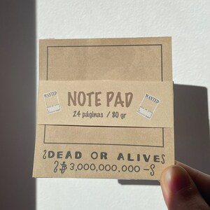 Puede incluir: Un bloc de notas de papel marr&oacute;n con un dise&ntilde;o de cartel de se busca. El bloc de notas tiene 24 p&aacute;ginas y pesa 80 gramos. El texto en el bloc de notas dice "Note Pad" y "&iquest;Dead or Alives $3,000,000,000-$"