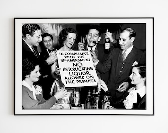 May include: Black and white photograph of a group of people holding a sign that reads "In compliance with the 18th Amendment, No intoxicating liquor allowed on the premises". The people are smiling and holding glasses of liquor.