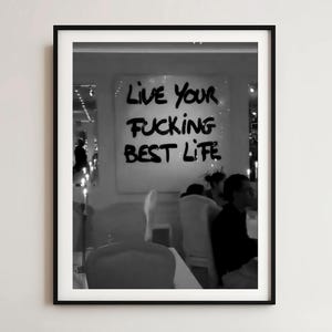 以下が含まれることがあります： 手書き風の「LIVE YOUR FUCKING BEST LIFE」というテキストが入った、白黒のフレーム入りプリント。レストランのシーンで、テーブルに座っている人々が描かれています。