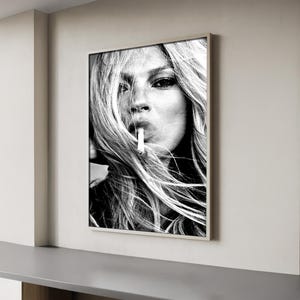 May include: Black and white framed print of a woman with long, flowing hair, smoking a cigarette. The portrait is a close-up, emphasizing the woman's face and the cigarette in her mouth. The image is in a minimalist style.