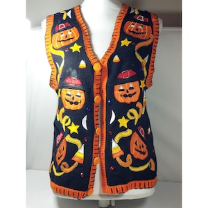 May include: Black sleeveless sweater vest with orange and white embroidered pumpkins, stars, and candy corn.
