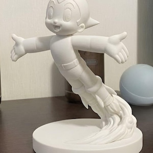 May include: A white figurine of a cartoon character in a flying pose, with arms outstretched. The figure is attached to a round base, with a rocket-like design emanating from the feet. The figurine is made of a solid, smooth material.