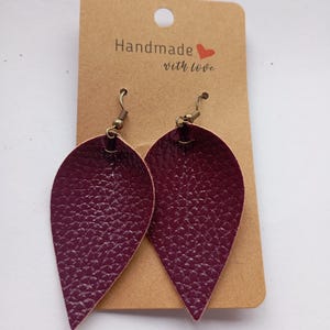 May include: A pair of teardrop-shaped earrings in a deep burgundy colour with a textured finish. The earrings feature bronze-toned metal hooks and are attached to a rectangular brown cardboard display card printed with the text Handmade with love.