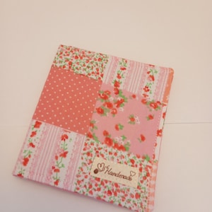 May include: A square fabric cover featuring a patchwork design of pink, white, and red floral, polka dot, and striped patterns. A small rectangular beige label is stitched to the front with the text Handmade and two small heart icons.