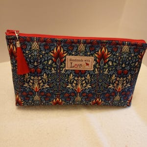 May include: A rectangular cosmetic bag with a red zip and tassel. The bag has a blue floral pattern with red and yellow accents. A small label reads "Handmade with Love."