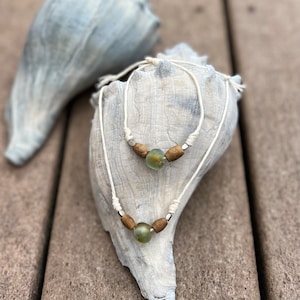 May include: Two necklaces with green glass beads and brown wooden beads on a white seashell background.
