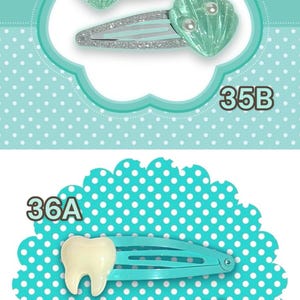 May include: A collection of hair clips with various designs. Includes red Hello Kitty clips, sea shell clips, tooth-shaped clips, and strawberry clips. Each set is displayed on a decorative background.