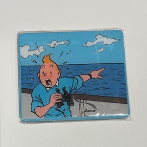 Pu&ograve; includere: Un sottobicchiere rettangolare con un'illustrazione a cartoni animati di Tintin, con la bocca aperta per la sorpresa, che indica il mare mentre tiene un binocolo. Lo sfondo mostra un cielo blu con nuvole e onde.