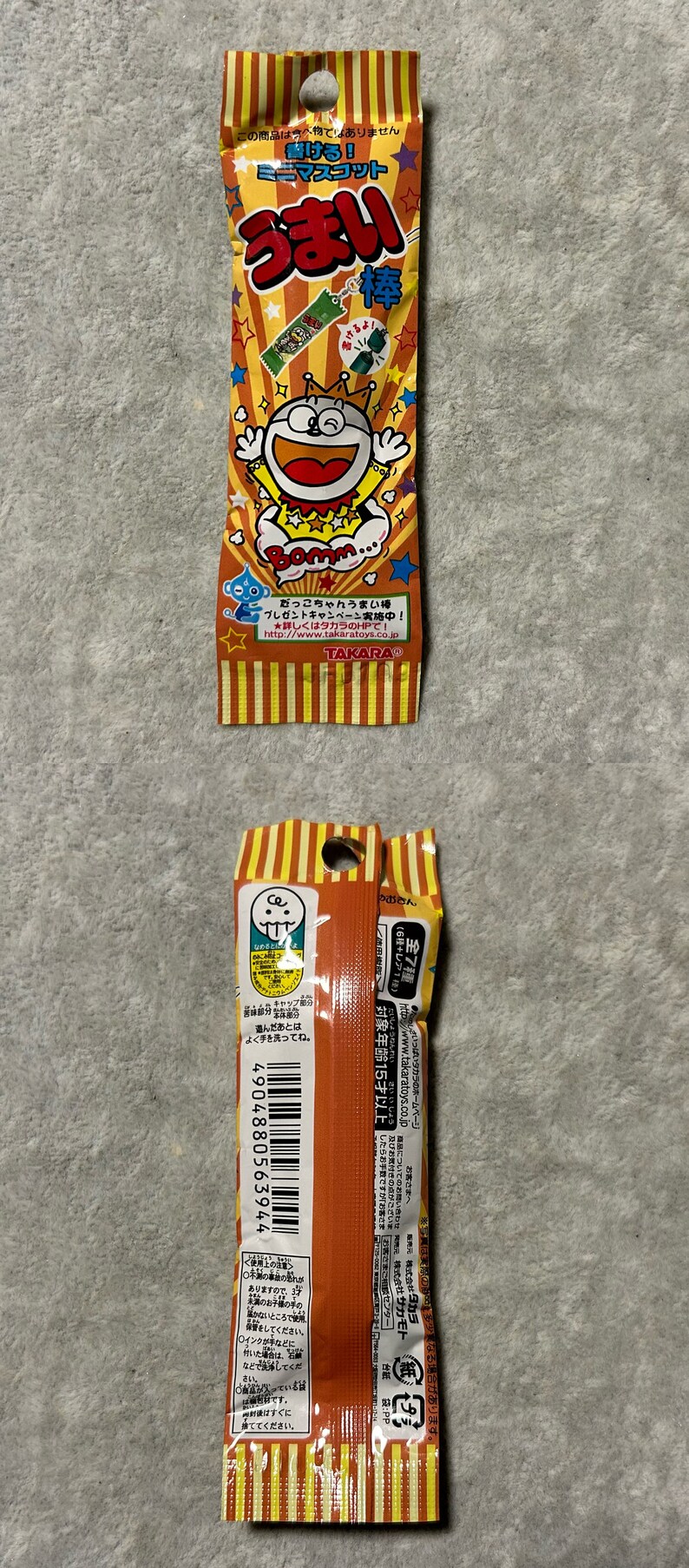 Pu&ograve; includere: Una confezione di snack giapponesi Umaibo. La confezione arancione e gialla presenta un personaggio dei cartoni animati e testo giapponese. Lo snack &egrave; un soffio di mais cilindrico.