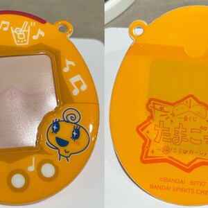 Pu&ograve; includere: Un giocattolo virtuale Tamagotchi giallo con schermo, note musicali e un personaggio dei cartoni animati. Il retro presenta testo giapponese e un logo. Il giocattolo &egrave; in plastica e ha un anello per attaccarlo a un portachiavi.