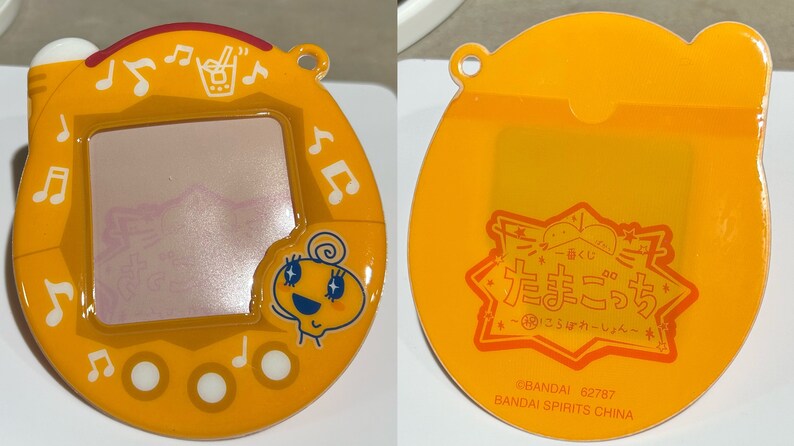 Pu&ograve; includere: Un giocattolo virtuale Tamagotchi giallo con schermo, note musicali e un personaggio dei cartoni animati. Il retro presenta testo giapponese e un logo. Il giocattolo &egrave; in plastica e ha un anello per attaccarlo a un portachiavi.
