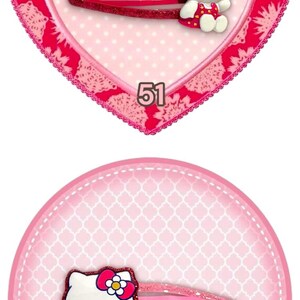 May include: A collection of four hair clips featuring cartoon characters. The clips include Hello Kitty and a teddy bear. The clips are in various colors, including black, pink, and purple. Each clip is set against a decorative background.