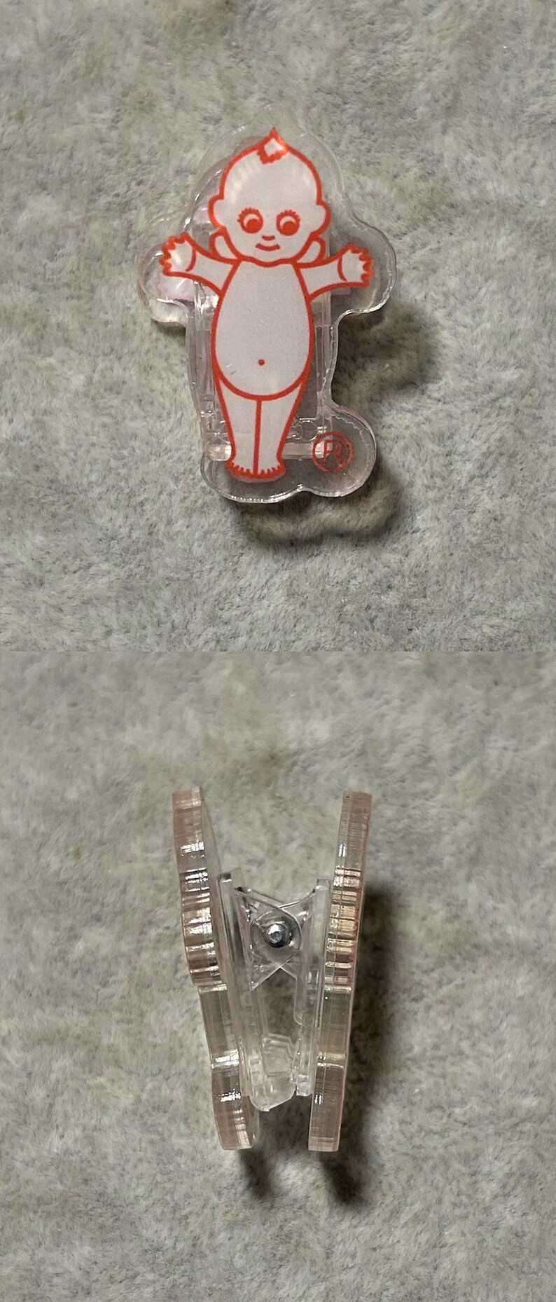 Pu&ograve; includere: Clip in plastica trasparente con un disegno di un bambino dei cartoni animati con contorni rossi. Il bambino ha le braccia tese e sorride. La clip &egrave; mostrata da due angolazioni, dall'alto e di lato.