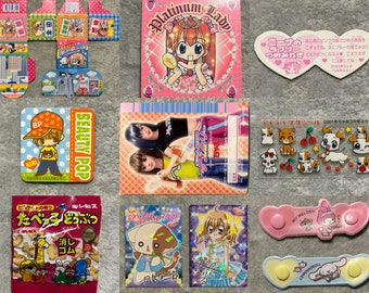May include: A collection of Japanese stationery and novelty items, including stickers, cards, and small containers. The items feature cartoon characters and colorful designs, with text in Japanese.