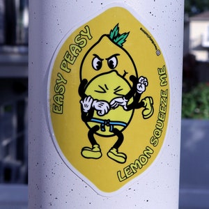 May include: A yellow sticker with a cartoon lemon character. The lemon is wearing a blue belt and has a grumpy expression. The text on the sticker reads "Lemon Squeeze Me Easy Peasy".