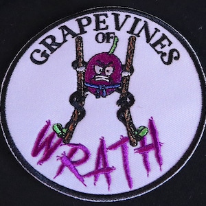 Puede incluir: Un parche circular blanco con un contorno negro. El parche presenta una uva morada de dibujos animados con una expresión gruñona, sujetando dos palos marrones. El texto "GRAPEVINES OF WRATH" está escrito en negro alrededor de la uva.