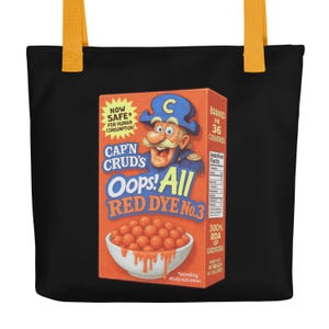 May include: Black tote bag with yellow straps featuring a parody cereal box design. The box is orange with a cartoon captain and the text "CAP'N CRUD'S Oops! All RED DYE No.3". Additional text includes "NOW SAFE for human consumption!" and "BANNED in 36 countries".