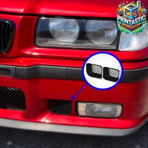 May include: A pair of black rectangular mesh grille inserts for a red vehicle bumper. The inserts feature a diamond-patterned grid design and are shown installed in the lower front bumper section, with a circular inset highlighting the parts.