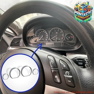May include: A car dashboard with a black steering wheel and silver gauge rings. The gauge rings are shown in a circle. The dashboard has several gauges and dials. The text "Gauge rings only - not instrument cluster" is visible. The image is a close-up.