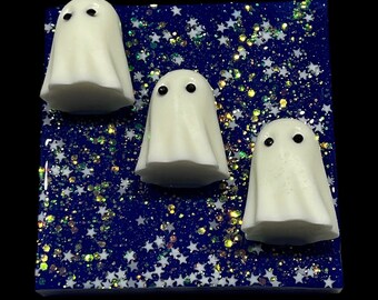 May include: Three white ghost figurines with black eyes on a blue background with white glitter stars.