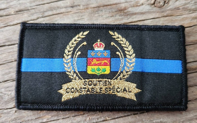 K&ouml;nnte beinhalten: Gestickter schwarzer Aufn&auml;her mit blauem Streifen und goldenen Akzenten. Mit Wappen, Krone, Wappen und dem Text "SOUTIEN CONSTABLE SPECIAL" in Gold. Rechteckige Form.