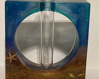 Puede incluir: Jarrón cuadrado de resina con un tubo de vidrio transparente en el centro. El jarrón tiene un diseño de brillo azul y dorado con una estrella de mar en la parte inferior.