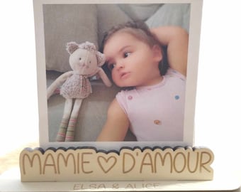 May include: A wooden photo frame with a white mat and a photo of a baby girl with a stuffed animal. The frame has a wooden inscription that reads "Mamie d'Amour Elsa & Alice".