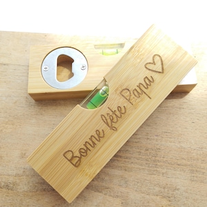 May include: A wooden bottle opener and spirit level combination. The bottle opener has a silver metal opener and a level with a green liquid. The level is in a wooden box with the words "Bonne fête Papa" and a heart symbol.