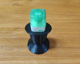 May include: A black 3D printed stand with a round top and a base that resembles a vase. A small green bottle with a white label is sitting on the stand.