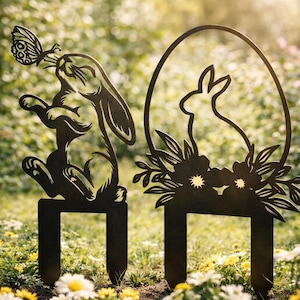 May include: Two black metal garden stakes. One features a rabbit with a butterfly on its nose, the other a rabbit silhouette inside an egg shape with floral accents. Both have a rectangular base for easy placement in the garden.