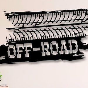 May include: Black metal wall art featuring tire tracks and the words "OFF-ROAD" in a stylized font. The artwork is mounted on a white wall above a wooden cabinet and a mid-century modern chair.